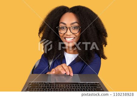 Cheerful black lady student typing at keyboard laptop and smiling on yellow background Cheerful black lady student typing at keyboard laptop and smiling on yellow background 110238928
