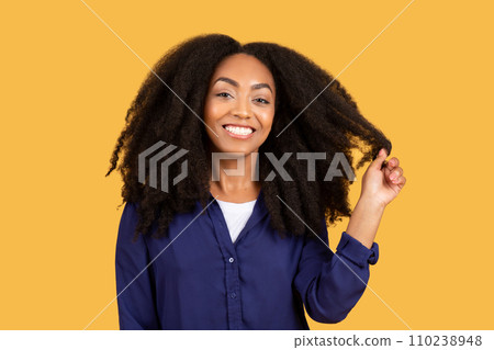 Happy african american woman touching her curly hair and smiling at camera over yellow studio background 110238948