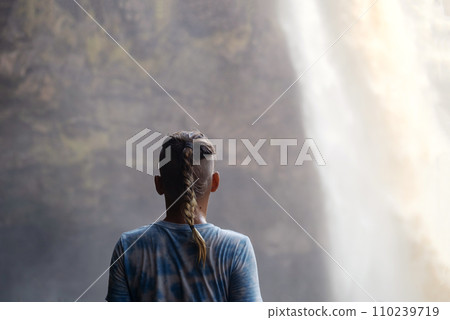 Teenager looking as waterfall cascades in front of him. 110239719