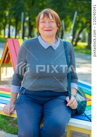 Portrait of a smiling mature woman, sitting on a bench 110240341