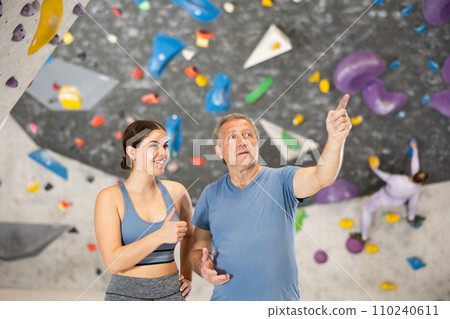 Adult man and young woman posing on climbing wall Adult man and young woman posing on climbing wall 110240611