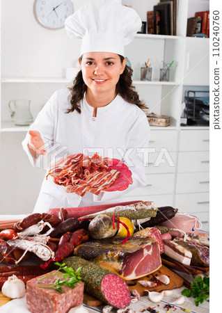 Girl cook costs near table on which sausages and smoked meat 110240760
