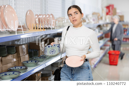 Young girl choosing with interest ceramic plates on shelves at Asian store Young girl choosing with interest ceramic plates on shelves at Asian store 110240772