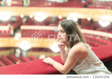 Young adult woman sitting alone on balcony of opera house 110241208