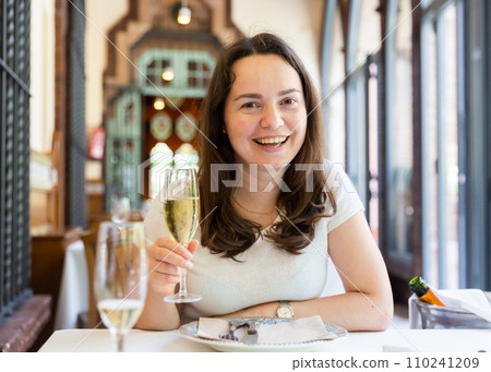 Positive woman holding glass of white wine in restaurant Positive woman holding glass of white wine in restaurant 110241209