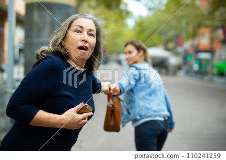Street thief trying to steal handbag of scared elderly woman Street thief trying to steal handbag of scared elderly woman 110241259