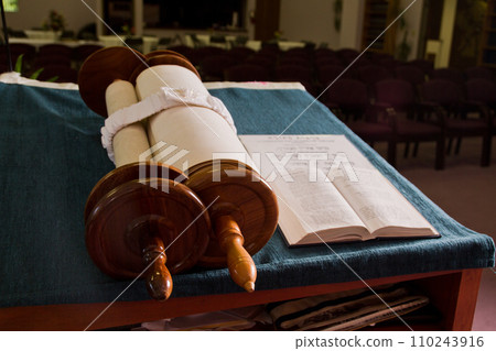 Torah Scroll on Blue Cloth with Empty Synagogue Chairs in Background 110243916