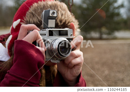 Woman Winter Hobbyist in Red Hat Capturing Moments with Vintage Film Camera in Outdoor Setting 110244185
