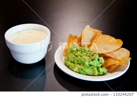 Close-Up of Mexican Appetizer - Tortilla Chips with Guacamole and Queso Dip on Dark Tabletop 110244207