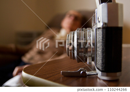 Vintage 35mm Film Camera on Wooden Surface with Blurred Old Man in Background Vintage 35mm Film Camera on Wooden Surface with Blurred Old Man in Background 110244266