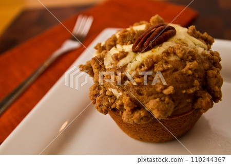 Close-Up View of Frosted Gourmet Apple Cheesecake Muffin with Pecan on White Plate 110244367