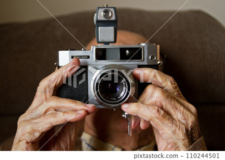 Elderly Old Mans Hands Holding Vintage Film Camera in Soft Indoor Lighting Elderly Old Mans Hands Holding Vintage Film Camera in Soft Indoor Lighting 110244501