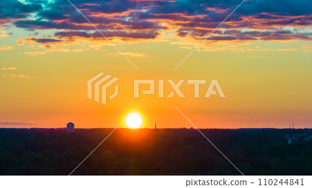 Pink and purple clouds with orange and yellow sky and setting golden sun on forest horizon aerial 110244841