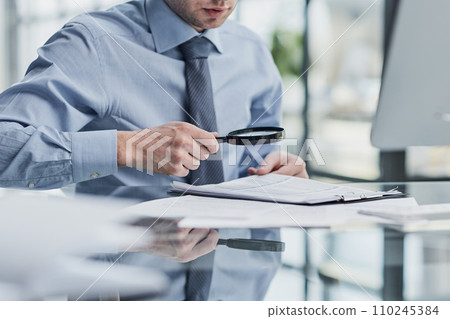 Businessman looking through a magnifying glass to documents Businessman looking through a magnifying glass to documents 110245384