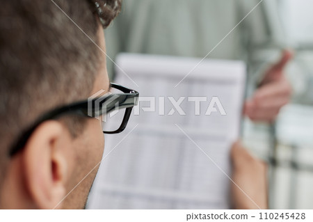 male accounting manager reviewing financial report, sitting at table alone at office 110245428