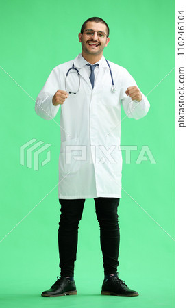 male doctor in a white coat on a green background rejoices. raised his hands up male doctor in a white coat on a green background rejoices. raised his hands up 110246104
