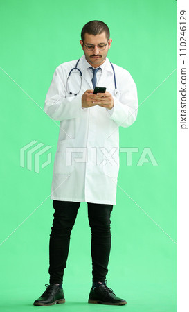 male doctor in a white coat on a green background looking at the phone male doctor in a white coat on a green background looking at the phone 110246129