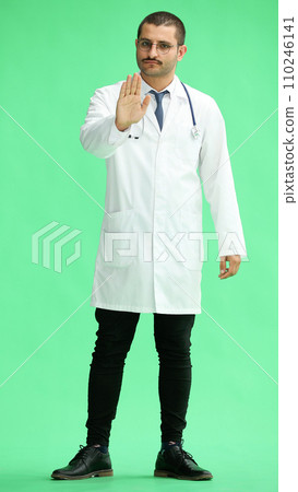 male doctor in a white coat on a green background shows a stop sign 110246141