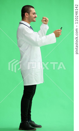 male doctor in a white coat on a green background looking at the phone male doctor in a white coat on a green background looking at the phone 110246142