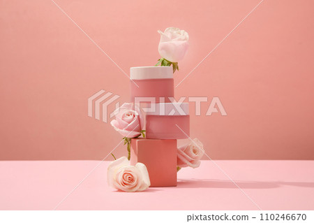 Two unlabeled cosmetic jars are placed on top of each other on a platform with decorative roses. Delicate pink background for cosmetics advertising. 110246670