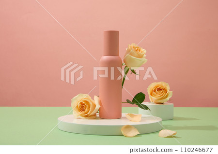 Close up of an unlabeled mineral spray bottle displayed on a white podium against a pink background with fresh roses. Cosmetic advertising space. 110246677