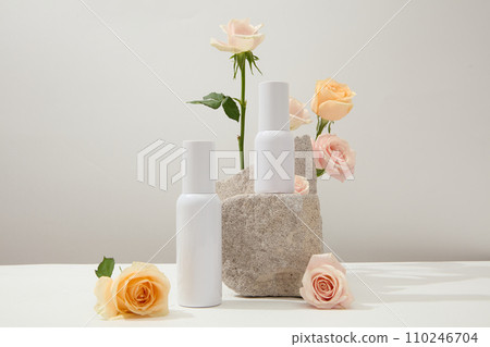 Unlabeled white cosmetics set displayed on a white background with fresh roses and a stone podium. Space with front view for cosmetics advertising. 110246704