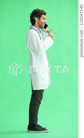 male doctor in a white coat on a green background speaks on the phone male doctor in a white coat on a green background speaks on the phone 110247140