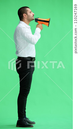 man isolated on a green background in business clothes with a loudspeaker in his hand man isolated on a green background in business clothes with a loudspeaker in his hand 110247169