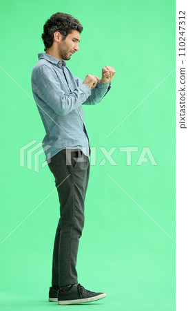 young man in full growth. isolated on green background looking at wristwatch young man in full growth. isolated on green background looking at wristwatch 110247312