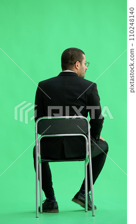 young man in full growth. isolated on a green background sitting on a chair young man in full growth. isolated on a green background sitting on a chair 110248140