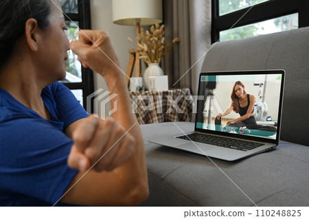 Cropped shot of senior woman exercising at home and watching tutorial training videos online on laptop. 110248825