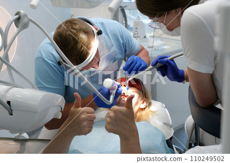 professional teeth cleaning in a dental clinic, removing stones and plaque, applying paint to teeth so that a layer of stones is visible, special newest devices in dentists, blue gloves, blue suits professional teeth cleaning in a dental clinic, removing stones and plaque, applying paint to teeth so that a layer of stones is visible, special newest devices in dentists, blue gloves, blue suits 110249502