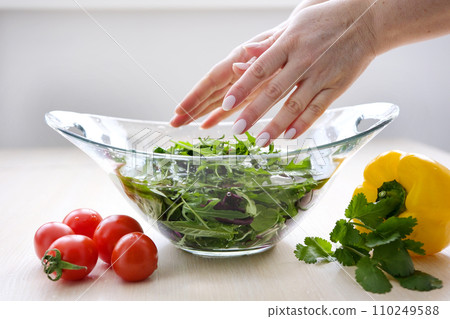 female hands toss a salad in a glass plate to the top next to there are tomatoes pepper and cilantro colorful leaves for cooking diet vegetarian food Cherry tomatoes female hands toss a salad in a glass plate to the top next to there are tomatoes pepper and cilantro colorful leaves for cooking diet vegetarian food Cherry tomatoes 110249588
