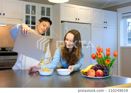 Loving daughter help mother and brother prepare breakfast before school. Healthy eating at home. Pleased teen girl pulls bottle of milk out of fridge for cornflakes. Happy family morning table time. Loving daughter help mother and brother prepare breakfast before school. Healthy eating at home. Pleased teen girl pulls bottle of milk out of fridge for cornflakes. Happy family morning table time. 110249639
