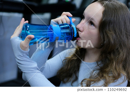 Portrait of sports woman with water. beautiful strong muscular woman drinking water in gym. young woman in grey sportswear with bottle of water. Fit thin gimnast sitting on stairs 110249692