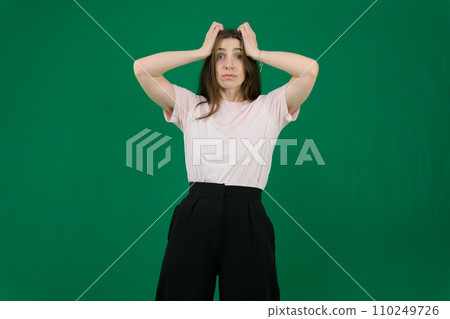 Portrait of a knee-high young pretty brunette girl woman with beautiful long hair on a green background in a white jacket and gray pants. She talks, shows hands with emotions in various poses. 110249726