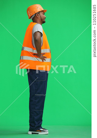 A male construction worker, on a green background, holds his hands on his belt, in profile A male construction worker, on a green background, holds his hands on his belt, in profile 110251685