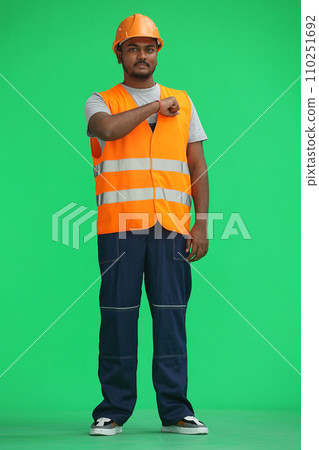A male construction worker, on a green background, in full height, punches his chest A male construction worker, on a green background, in full height, punches his chest 110251692