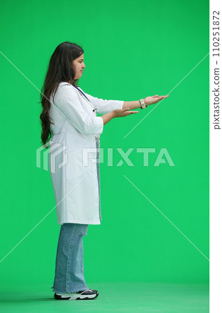 A female doctor, on a green background, in full height, points to the side, profile 110251872