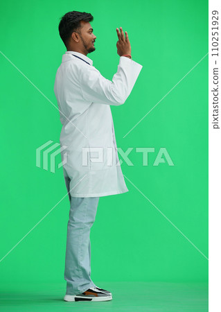 A male doctor, on a green background, in full height, shows the ok sign, profile 110251929