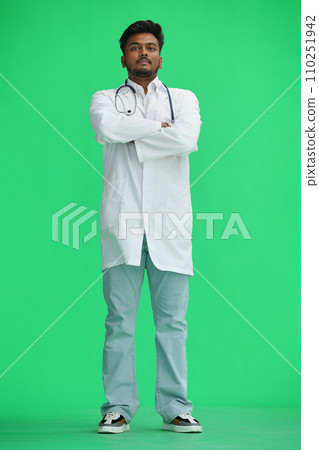 The male doctor, on a green background, in full height, crossed his arms 110251942