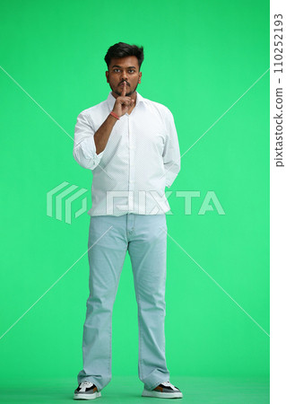 A man in a white shirt, on a green background, in full height, shows a sign of silence 110252193