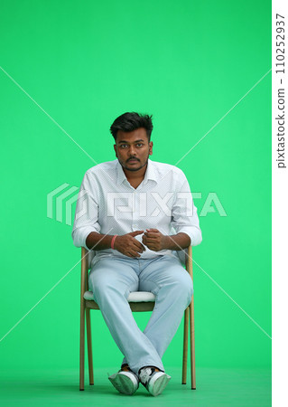 A man in a white shirt, on a green background, sitting on a chair A man in a white shirt, on a green background, sitting on a chair 110252937