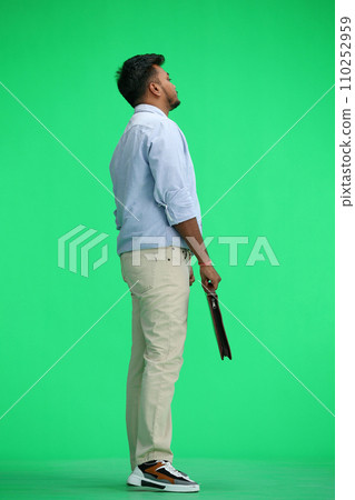 A man in a blue shirt, on a green background, full-length, with a briefcase in his hands, in profile 110252959