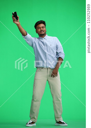 A man in a blue shirt, on a green background, in full height, waving his phone 110252989