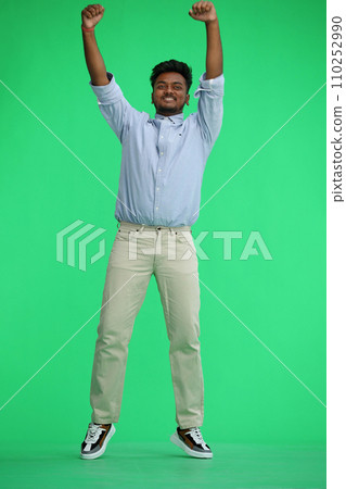 A man in a blue shirt, on a green background, in full height, shakes his hands over himself 110252990