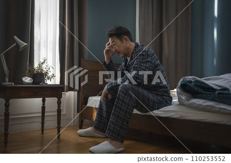 Middle-aged man sitting on bed and holding his head 110253552