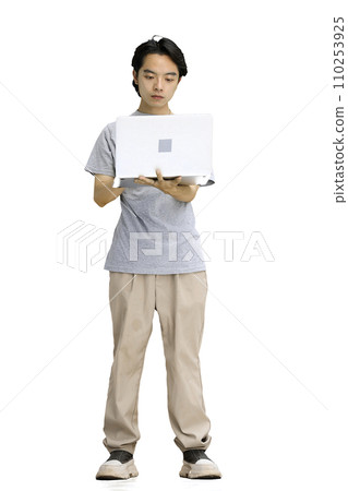 A guy in a gray T-shirt, on a white background, in full height, uses a laptop 110253925