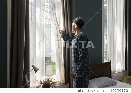 一名50多歲的男子穿著睡衣拉開臥室的窗簾 110254170