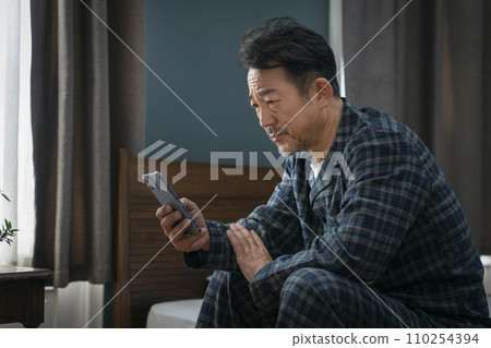 Middle-aged man looking at his smartphone with a gloomy expression Middle-aged man looking at his smartphone with a gloomy expression 110254394